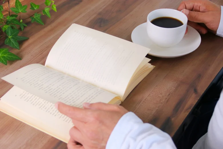 木製デスクでコーヒーを飲みながら読書している男性